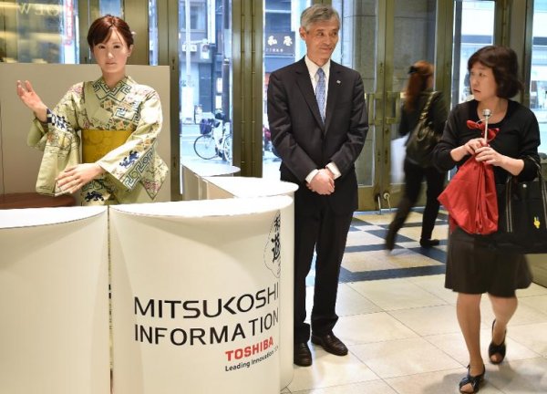 Humanoiden ChihiraAico, klädd i en japansk kimono, hälsar en kund välkommen vid en ingång till ett varuhus i Tokyo